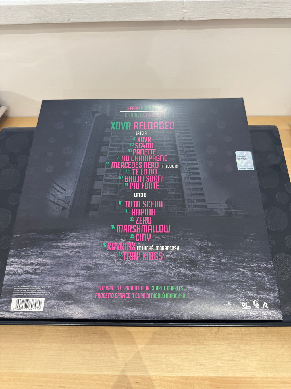 Retro copertina XDVR Reloaded - tracklist completa Lato A e Lato B su sfondo dark con pioggia, prodotto da Charlie Charles, grafica Nicolò Mancuso, barcode Universal Music Italia