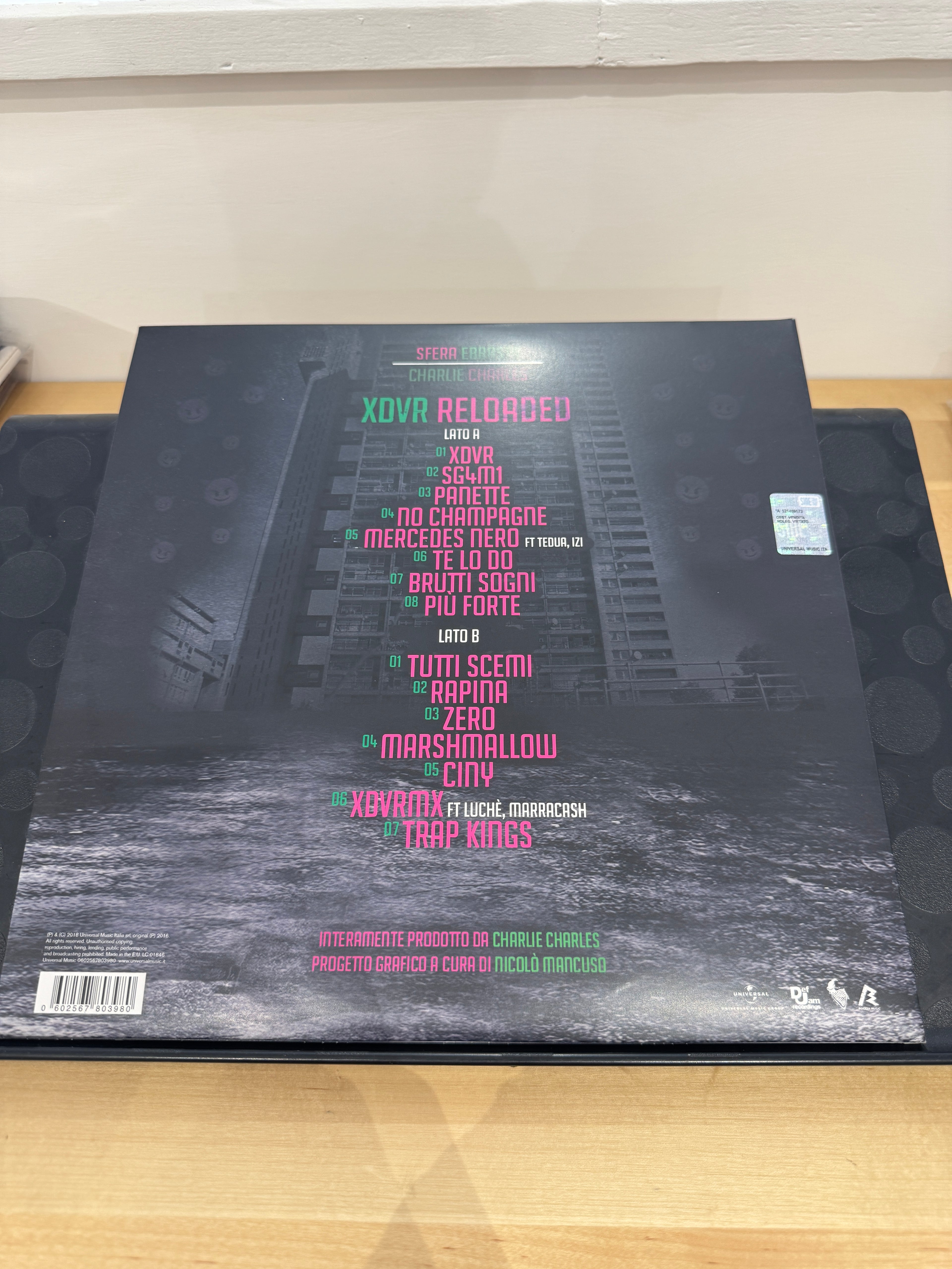 Retro copertina XDVR Reloaded - tracklist completa Lato A e Lato B su sfondo dark con pioggia, prodotto da Charlie Charles, grafica Nicolò Mancuso, barcode Universal Music Italia