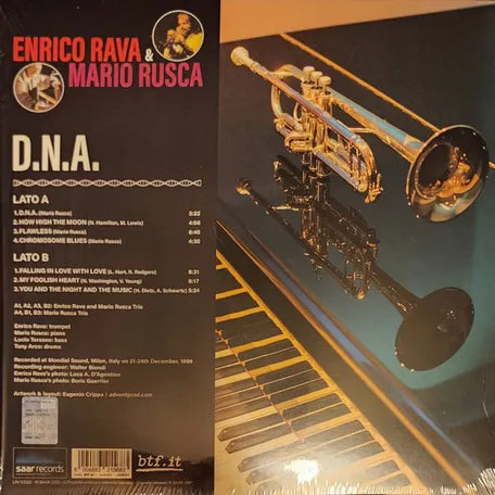 Copertina Enrico Rava Mario Rusca DNA SAAR Records - tromba dorata su pianoforte nero su sfondo grigio, scritta rossa ENRICO RAVA e rosa MARIO RUSCA a sinistra, scritta bianca D.N.A. a destra